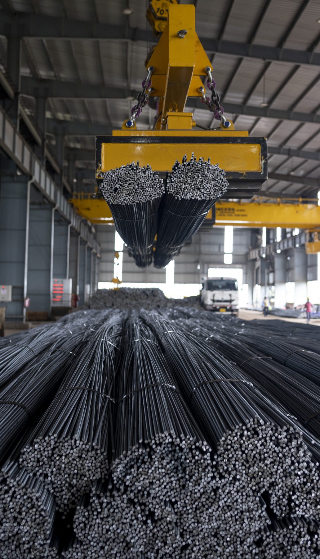 A crane lifting two bundles of rebar above stacked bars